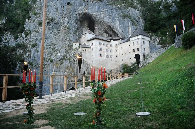 Predjama Castle in its cliff above a lawn set with flower-wrapped torches