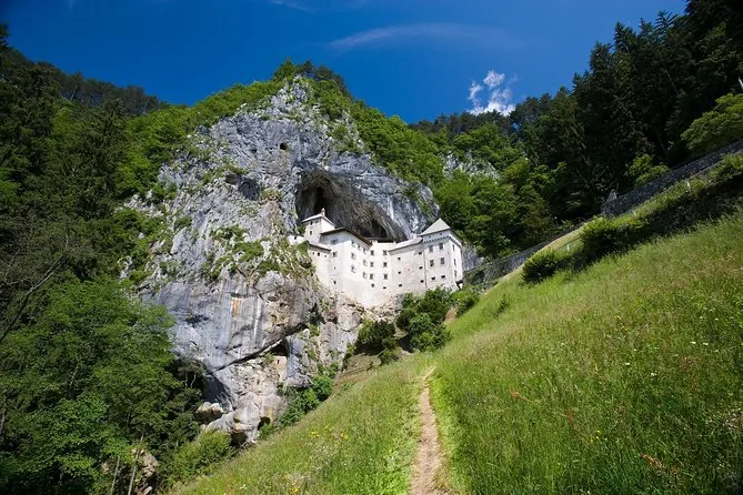 Predjama Castle seen from below, with a footpath through the grass leading up the slope