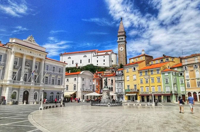 Piran's main square with its bell tower, a statue and pastel houses under a blue sky