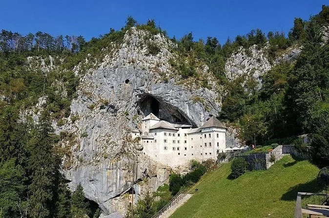 Die Burg Predjama und ihre Felswand, vom grünen Tal darunter aus gesehen