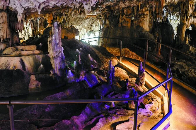 Farbige Beleuchtung an Stalaktiten über einem Weg mit Geländer in der Höhle