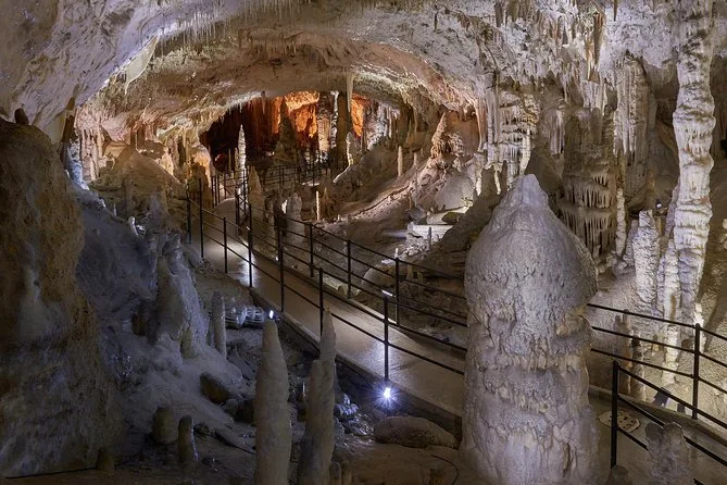 Un sendero con barandilla que serpentea entre estalagmitas claras bajo una bóveda de cueva